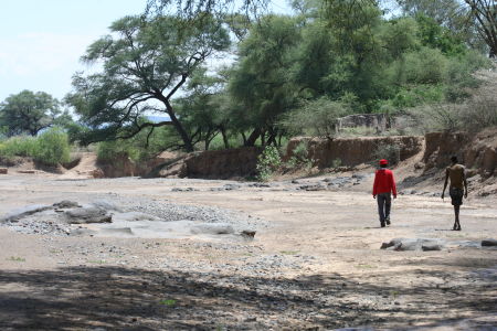 Two Pokot men walk down a dry riverbed